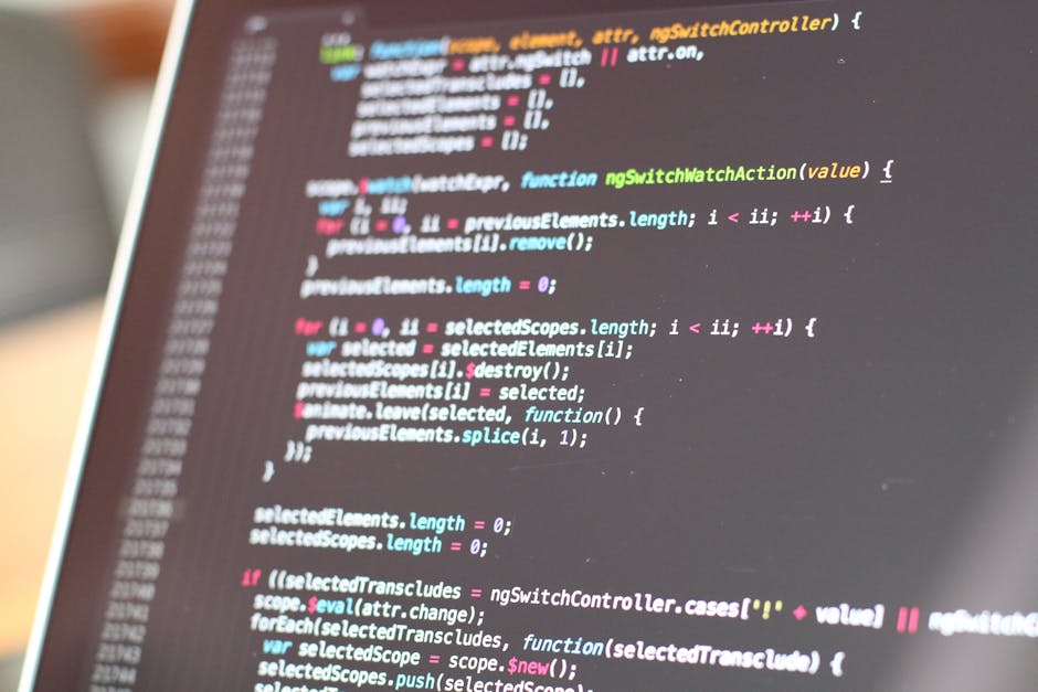 A close-up image of a laptop with a dark screen displaying lines of colourful coding, positioned on a wooden desk. To the right of the laptop, there is a ceramic coffee mug with a cream background and